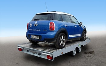 Blauer Mini auf Autotransporter mit kippbarem Plateu auf Straße, von hinten gezeigt