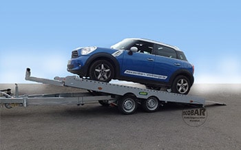 Blauer Mini auf kippbarem Autotransporter auf Straße, seitlich gezeigt